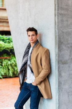 Portrait of stylish handsome young man standing outdoors and leaning on wall.