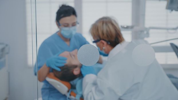 Team of experts performing oral care procedure with drill instrument in stomatology office. Orthodontist and assistant using dental tools and equipment at consultation with patient.