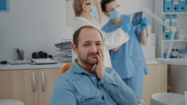 Portrait of patient with toothache looking at camera in dentistry office. Man in pain having stomatological appointment to do extraction procedure, feeling hurt because of caries problems.