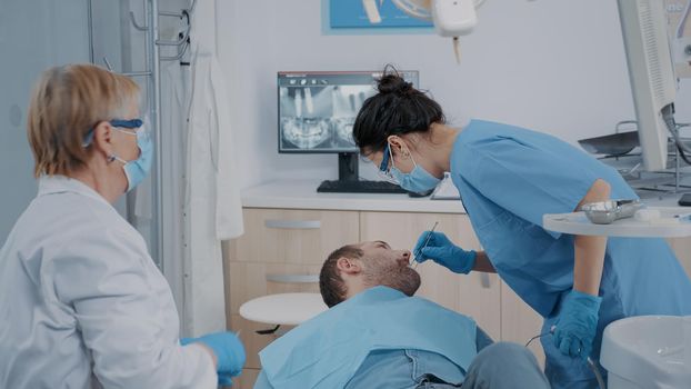 Stomatologist and nurse doing extraction procedure on patient with toothache. Team of specialists using dental tools to perform surgery at stomatological examination in dentistry office.