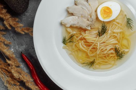 Chicken soup with noodles and vegetables in white bowl.