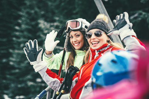 Beautiful young woman friends enjoying in winter vacations. They driving on ski lift and looking at camera with smile.