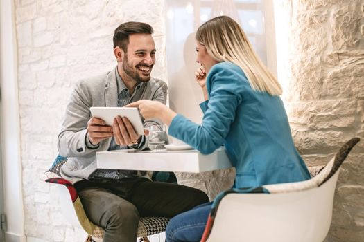 Two beautiful young smiling people sitting at cafe and working on digital tablet.