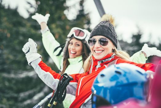 Beautiful young woman friends enjoying in winter vacations. They driving on ski lift and looking at camera with smile.