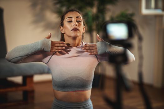 Young beautiful sporty woman vlogger is making video training for blog about healthy living and exercises in front of a camera at home. 