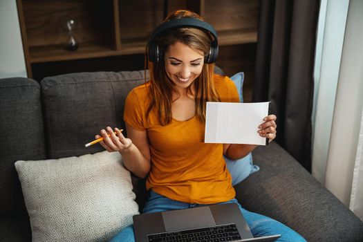 Cute young female student using a laptop and headphones and learning at home.