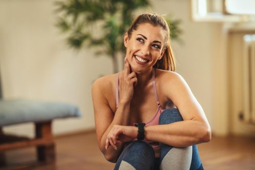 Young woman is checking heart rate during sports training in the living room at home. She is measuring heart rate on her neck and looking at smartwatch.