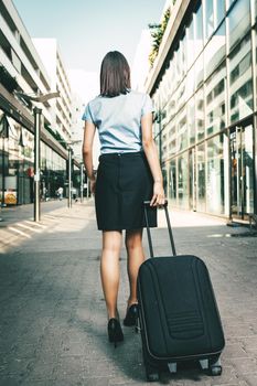 Young beautiful businesswoman standing outdoor with suitcase ready for a business trip.