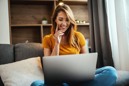 Shot of an attractive young woman sitting cross legged on the sofa and using her laptop at home.