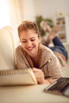 Beautiful young smiling woman relaxing by drawing in a sketchbook with colored pencils at home. 