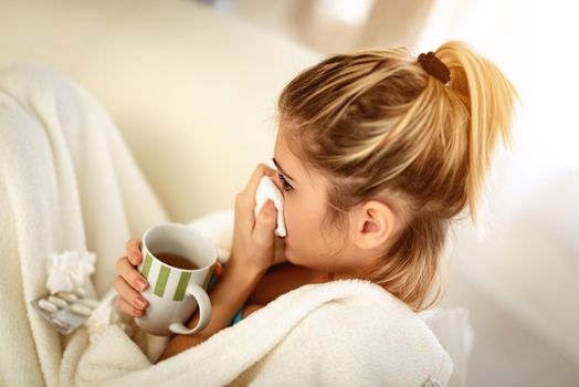 A beautiful girl with handkerchief to her nose and holding a cup of tea.