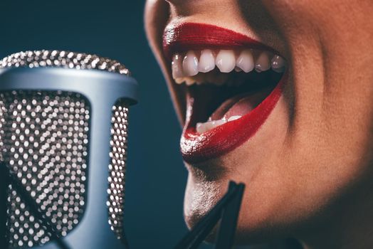Close-up of a female open mouth with red lipstick singing on the microphone.