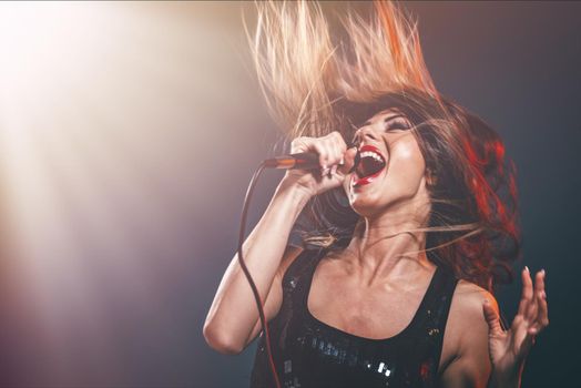 A young woman singer with tousled long hair holding a microphone and sing with a wide open mouth.