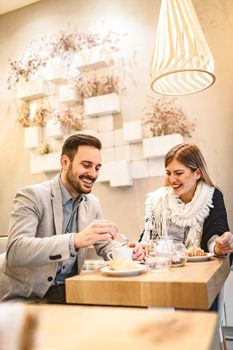 Young man and young woman sitting at cafe and talking with smile. They drinking coffee and having breakfast.