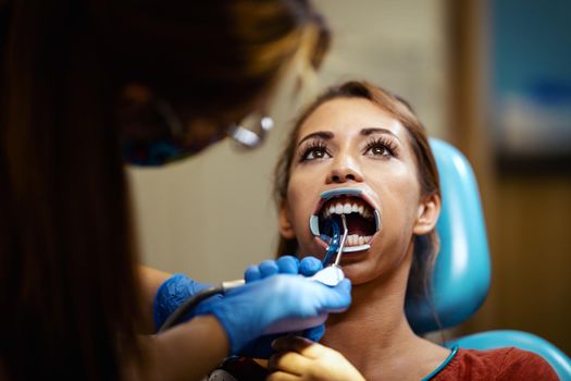 The beautiful young woman is at the dentist. She sits in the dentist's chair and the dentist sets braces on her teeth putting aesthetic self-aligning lingual locks.