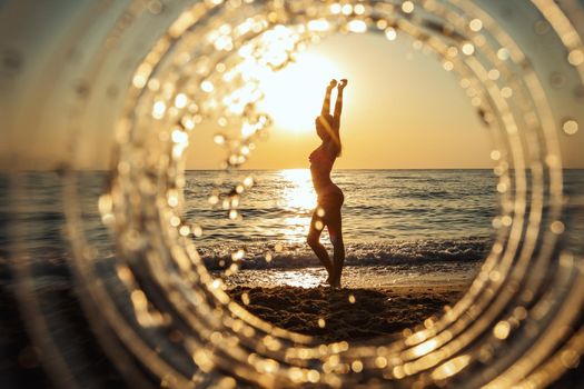 A beautiful creative composition of a sea landscape shot through a circle focus showing a teenage girl who posing on the beach in sunset.