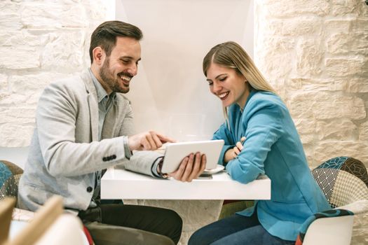 Two beautiful young smiling people sitting at cafe and working on digital tablet.