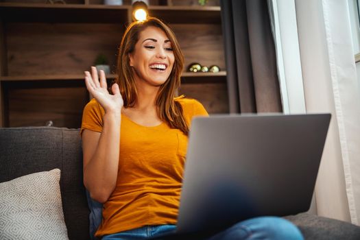 Attractive young woman using her laptop to make a video call with someone at home.