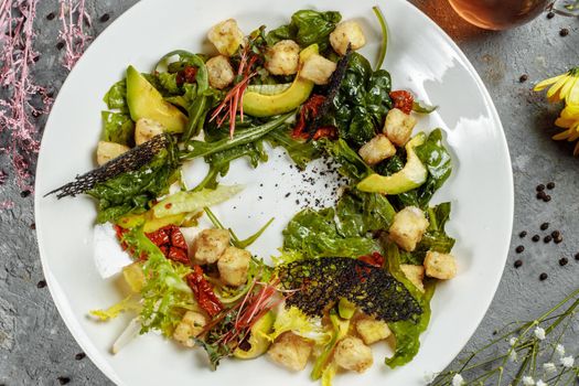 Avocado salad with baby spinach and pomegranate on a black plate on a slate,stone or concrete background.Top view with copy space.