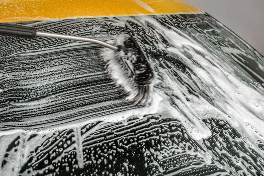 Windshield of yellow car washed in carwash, brush leaving strokes in white shampoo and foam.
