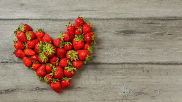 Tabletop view, strawberries on wood desk, arranged in shape of heart, space for text right.