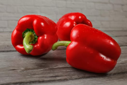 Three bright red bell peppers on wooden desk, focus to water drops.