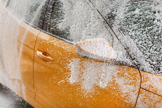 Side of a car, washed in self serve carwash, wind shield and mirror covered with shampoo and foam.