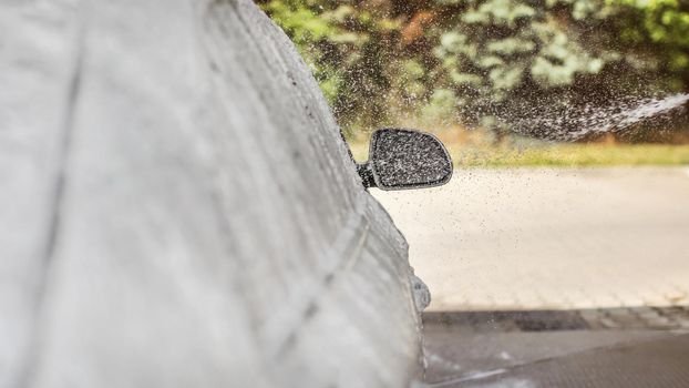 Shampoo foam and water spray falling on side mirror of a car washed in self service carwash. Focus to drops only, left is place for text.