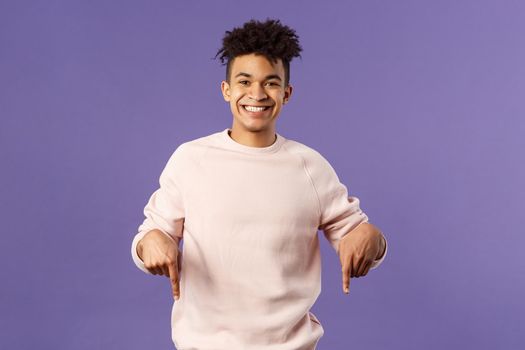 Portrait of cheerful, happy young 25s man recommending product, showing promo of product, delivery service, online shop or appllication, pointing fingers down, smiling pleased camera.