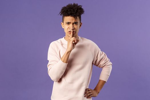 Portrait of disappointed, annoyed young bossy man trying work remote from home shushing at family talking too loud during his online video conference, hush with angry grimace.