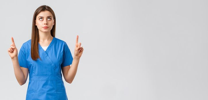 Healthcare workers, prevent virus, covid-19 test screening, medicine concept. Concerned, serious and focused female doctor or nurse in blue scrubs, pointing fingers and looking up at banner.