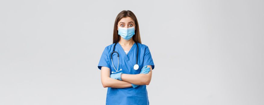 Covid-19, preventing virus, health, healthcare workers and quarantine concept. Amused female doctor or nurse in blue scrubs with stethoscope and personal protective equipment look intrigued.