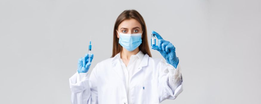 Covid-19, preventing virus, healthcare workers and quarantine concept. Doctor in medical mask, rubber gloves and scrubs showing ampoule with coronavirus vaccine, hold syringe, making patient a shot.