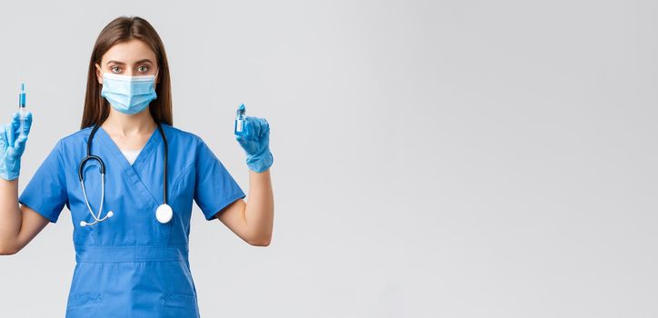 Covid-19, preventing virus, healthcare workers and quarantine concept. Confident, professional female doctor, nurse in clinic wearing scrubs and medical mask, showing coronavirus vaccine and syringe.