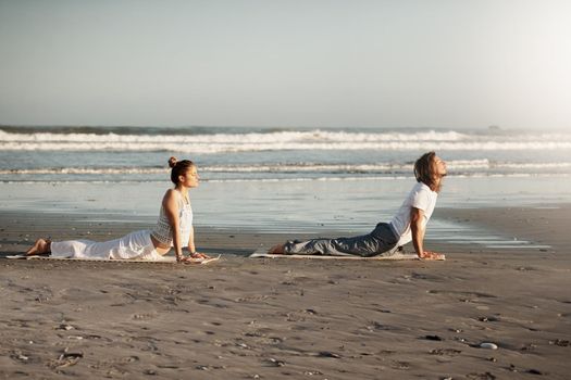 Shot of a young couple practising yoga together on the beach.