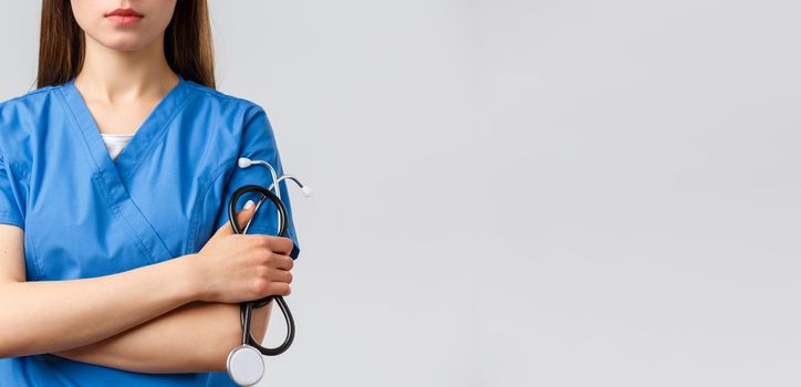 Healthcare workers, medicine, insurance and covid-19 pandemic concept. Cropped shot of young female doctor or nurse in blue scrubs with serious face, cross arms and hold stethoscope.