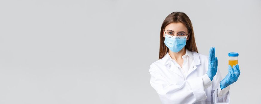 Covid-19, medical research, diagnosis, healthcare workers and quarantine concept. Doctor, intern in medical mask and gloves, lab clinic testing urine sample, show rejection and refusal gesture.