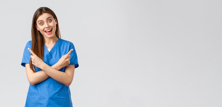 Healthcare workers, prevent virus, insurance and medicine concept. Enthusiastic smiling female nurse, doctor in blue scrubs, pointing fingers sideways left right, showing two products or banners.