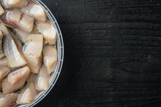 Sliced herring in oil marinated, on black wooden table background, top view flat lay with copy space for text