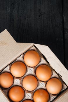 Brown eggs in carton box tray set, on black wooden table background, top view flat lay , with space for text copyspace