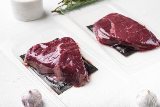 Vacuum black plastic pack with rump beef meat cut set, on white stone table background, with copy space for text