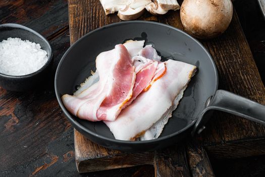 Sizzling bacon pieces set in cast iron frying pan, on old dark wooden table background