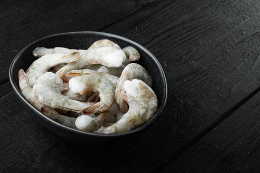 Frozen raw uncooked tiger prawns, shrimps set, on black wooden background, with copy space for text