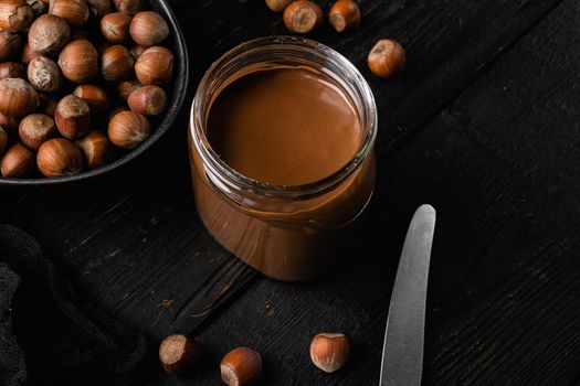 Chocolate spread or nougat cream with hazelnut set, on black wooden table background