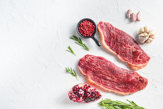 Two picanha beef steaks with rosemary and garnet, over white background, top view with space for text