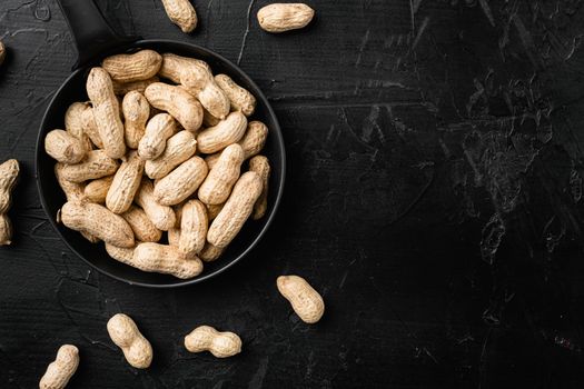 Organic peanuts in shell set, on black dark stone table background, top view flat lay, with copy space for text