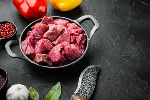 Raw organic meat beef or lamb set with sweet bell pepper, in cast iron frying pan, on black stone background, with copy space for text