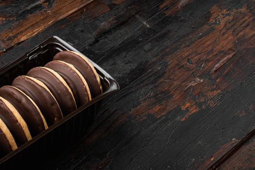 Chocolate coated biscuit cakes set, in plastic tray container, on old dark wooden table background, with copy space for text