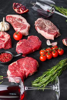 Rump, beef steak cuts,in front of top blade steak with herbs, seasoning and red wine glass on black table, side view