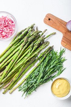 Raw asparagus eggs and french dressing ingredients with dijon mustard, onion chopped in red vinegar taragon on white textured background, top view